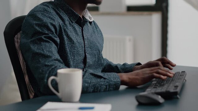 Black african american manager working from home, tuping on computer keyboard. Panning close up shot from hands to the face. Bright nice home office