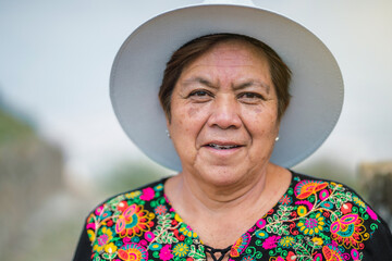 adult woman in hat looking at camera and smiling. he wears typical Mexican clothes