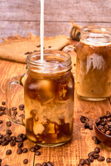 splash of iced latte macchiato coffee in a glass jar on a wooden table with coffee beans and jute cloth napkins. wooden background with copy space for advertising.