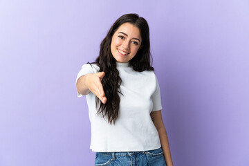 Young caucasian woman isolated on purple background shaking hands for closing a good deal