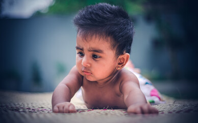 Crawling sweet baby girl in a reed mat looking at something confusingly. facial expressions of five months old cute crawling baby.