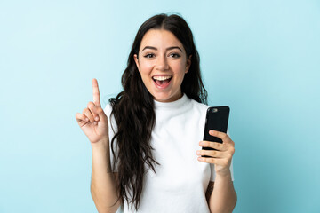 Young woman using mobile phone isolated on blue background pointing up a great idea