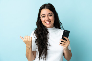 Young woman using mobile phone isolated on blue background pointing to the side to present a product