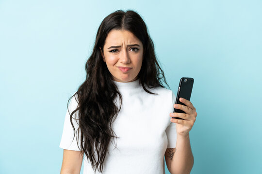 Young woman using mobile phone isolated on blue background with sad expression