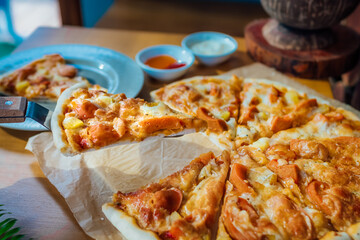 Homemade pizza on brown paper on wooden table with green leaf and white cream