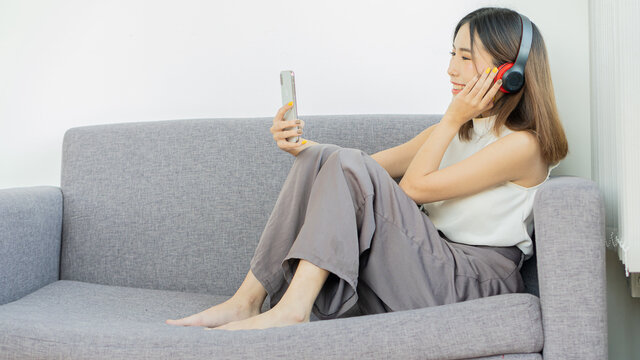 Girl Watching Movie Listen To Music On Your Cell Phone And Wear Headphones To Chat With Friends On The Couch Happily At Home.