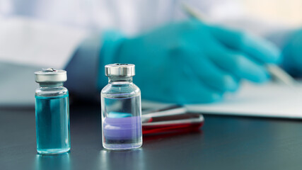 A bottle of vaccine placed in front of a doctor writing a prescription in the office.