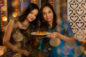 Obraz na płótnie Canvas Portrait of two Indian woman sharing sweets on the festive occasion of Diwali. Celebrations at home.