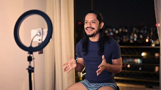 Latin youtuber filming a video for social media at home in the living room during night using a ring light and the smart phone