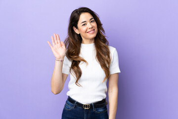 Woman over isolated purple background saluting with hand with happy expression