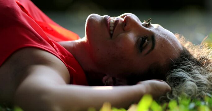 Relaxed hispanic woman lied on grass outside at park, person relaxing lying daydreaming