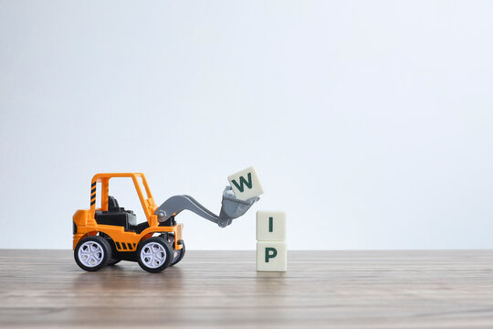 Work in progress concepts.  A toy bulldozer lifting white cubes with lettering on WIP.