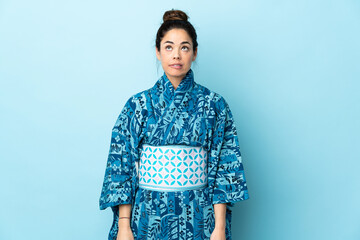 Woman wearing kimono over isolated background having doubts while looking up