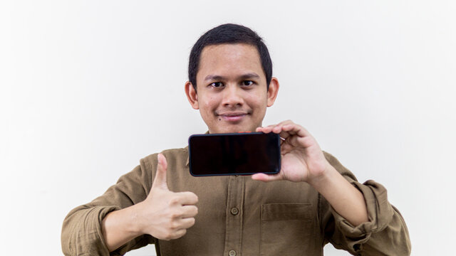 Young Asian Malay Man Showing Thumbs Up And Holding Smartphone With Empty Black Screen.