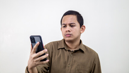 Serious and thoughtful face expression of young Asian Malay man looking at the smartphone.