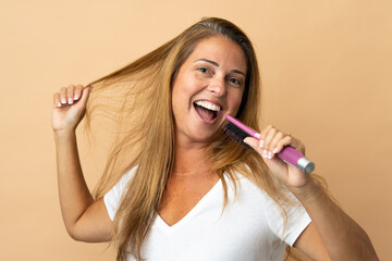 Middle age brazilian woman isolated on beige background with hair comb and singing