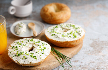 Breakfast table with bagels fresh cheese. Bagels with fresh cheese and herbs on a breakfast table , with fresh orange juice and coffee on the side.