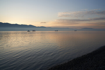 The sunrise over the calm sea casts rays of orange light into the air as the setting sun penetrates through the clouds into the picturesque calm seascape, the sea.