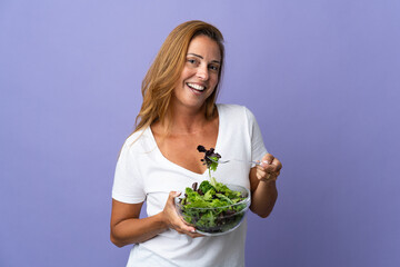 Middle age brazilian woman isolated on purple background holding a bowl of salad with happy expression