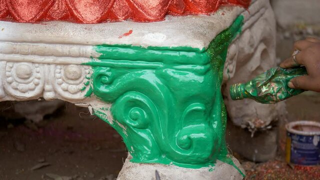 Female artist's hands spraying sparkles on the statue of a Hindu Goddess . Woman craftsperson putting glitters on the color for a shiny look of the clay sculpture of an Indian Goddess