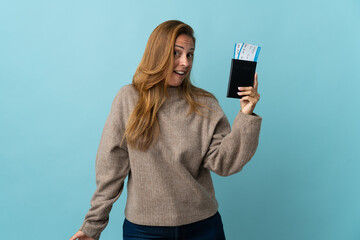Fototapeta premium Traveler middle age woman holding a suitcase isolated on blue background happy in vacation with passport and plane tickets
