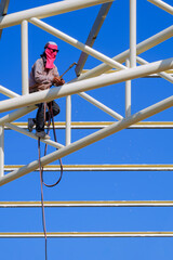 Low angle view of welder is welding roof metal structure of warehouse building in construction site...