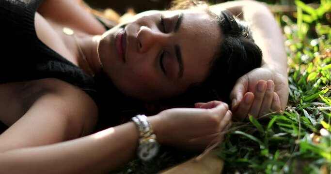 Woman opening eyes lied on grass outside daydreaming, relaxed girl