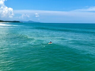 A young man surfer riding waves at Natai beach in Phang Nga, Thailand. Asian man catching waves in blue ocean. Surfing action water board sport.