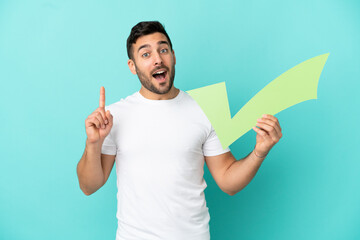 Young handsome caucasian man isolated on blue background holding a check icon and pointing up