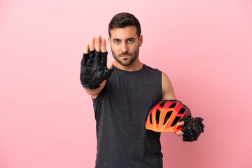 Young cyclist man isolated on pink background making stop gesture - obrazy, fototapety, plakaty