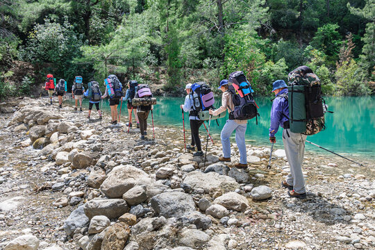 A group of tourists with large backpacks cross the river over the rocks in the goynuk canyon on the Lycian trail in Turkey