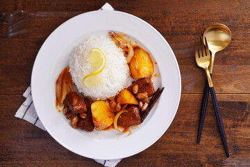 Thai food with rice Pork massaman curry with potatoes, peanuts, coconut milk and onions in a cup on a wooden table