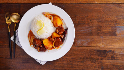 Thai food with rice Pork massaman curry with potatoes, peanuts, coconut milk and onions in a cup on a wooden table