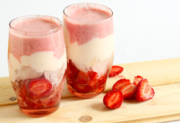 Milk strawberry cocktail made from fresh strawberries with ice cubes, whipped cream and strawberry pieces in two glass pink glasses on a wooden plank. Healthy food concept