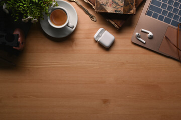 Top view modern workplace with laptop, notebook, wireless earphone, coffee cup and plant on wooden background.