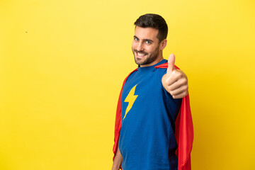Young handsome caucasian man isolated on yellow background in superhero costume with thumb up
