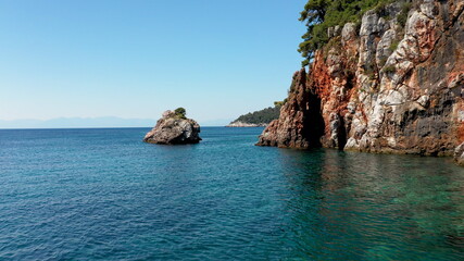 Fototapeta premium Aerial drone views over a rocky coastline, crystal clear Aegean sea waters, touristic beaches and lots of greenery in Skopelos island, Greece. A typical view of many similar Greek islands.