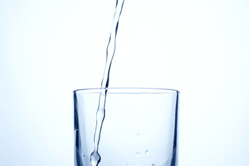 Jet of water or alcohol is pouring into a glass with splashes and bubbles, copy space