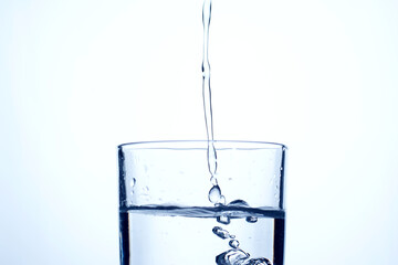 Jet of water or alcohol is pouring into a glass with splashes and bubbles, copy space