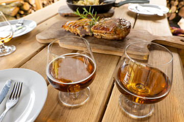 Meal, party in the foreground glasses with beer, brandy, in the background baked bacon lies on a wooden board, decorated with herbs