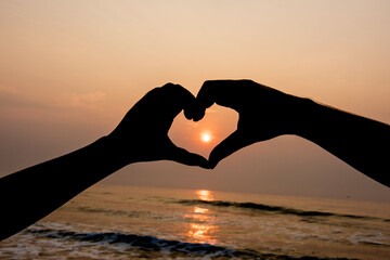 The silhouette made the heart shape from the hands at sunset.