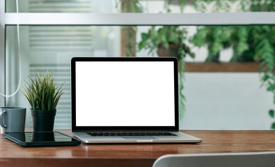 Mockup blank screen laptop computer on wooden table with green plant background.