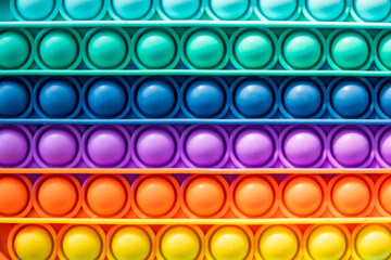 Bright rainbow toy antistress for children and adults on a colorful background. Flexible sensory antistress toy - popit.