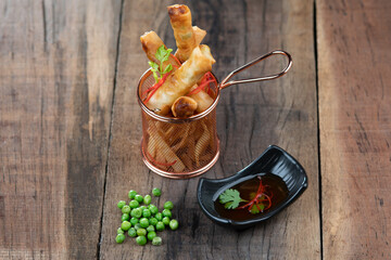 Chicken wrapped in rice paper with potato, green peas, onion served with a sweet chili palm sauce on the side isolated over wooden table