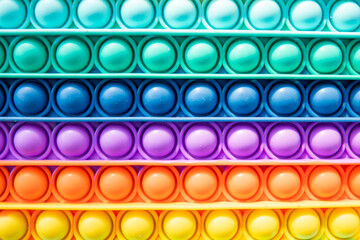 Bright rainbow toy antistress for children and adults on a colorful background. Flexible sensory antistress toy - popit.