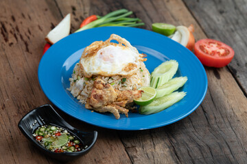 Fried rice with egg on top, pork crackling and cucumber isolated on rustic wooden table