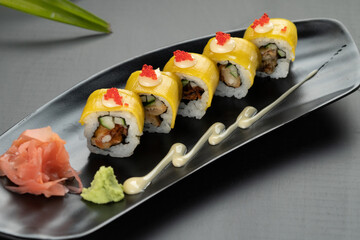 Deep-fried soft-shell crab, cucumber, mango, mayonnaise and tobiko isolated on black table with tropical leaves