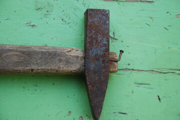 Old hammer with a wooden handle. An old straight iron hammer with a wooden handle lies on the background of painted green wood. There are traces of rust on the iron.