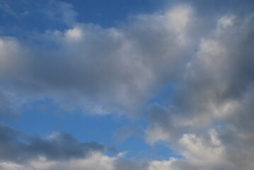 Multilevel clouds in the sky. In the light blue sky, clouds of different shapes and in different layers. Part of the clouds is white, part is gray from the shadow falling on them.