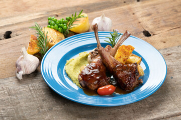 Two grilled lamb chops and potatoes served on pea puree with a mint sauce isolated on rustic wooden...